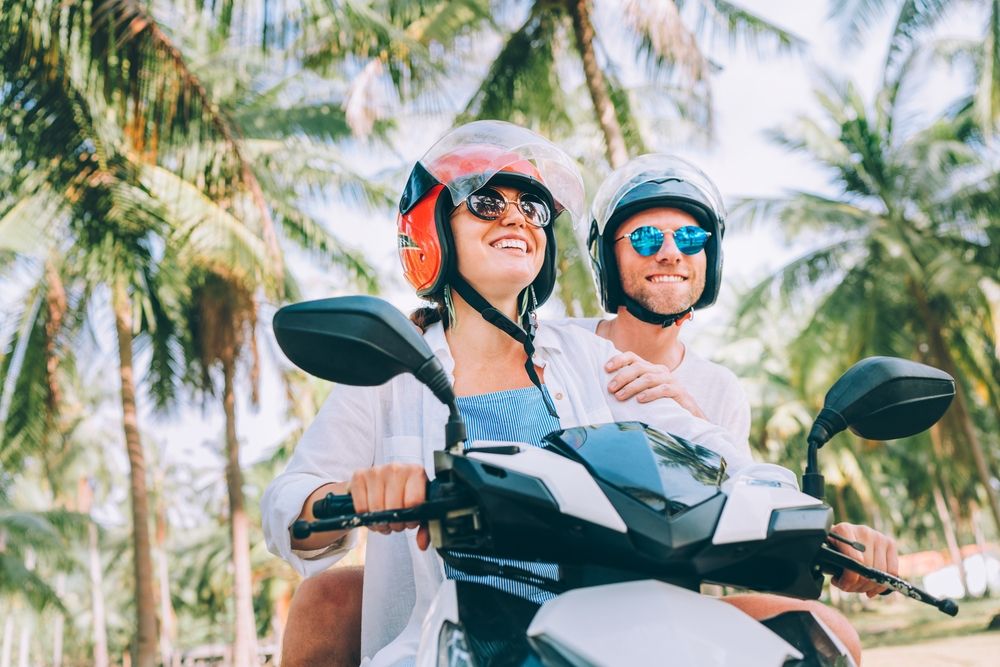 Happy smiling couple travelers riding motorbike scooter in polarized sunglasses helmets